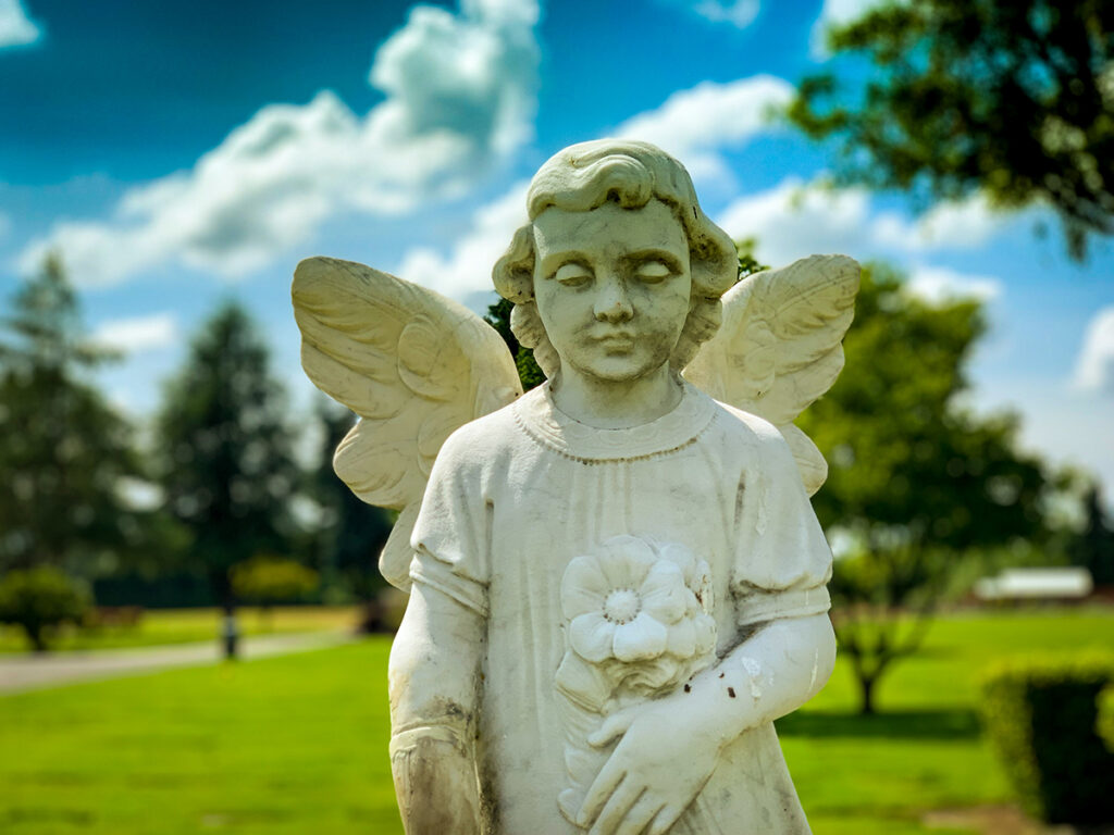 Angel statue looking down with green grass and blue sky behind. 