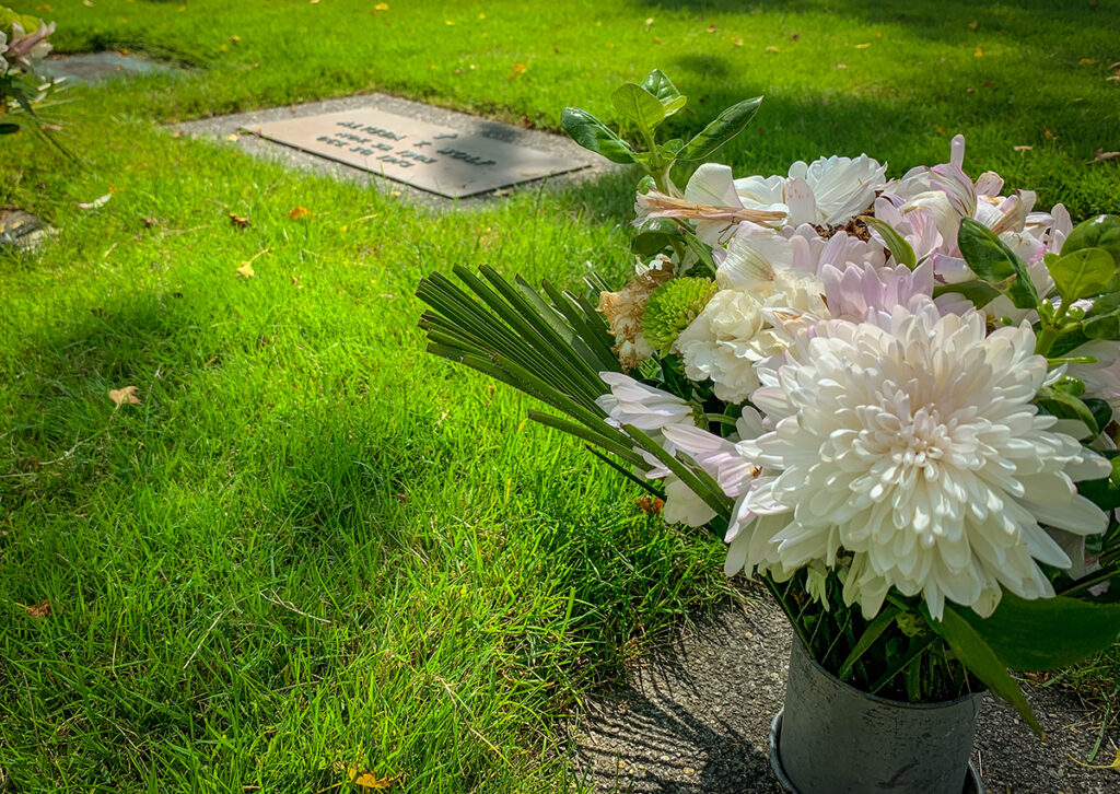 Flush marker in grass with a vase of white mums. 