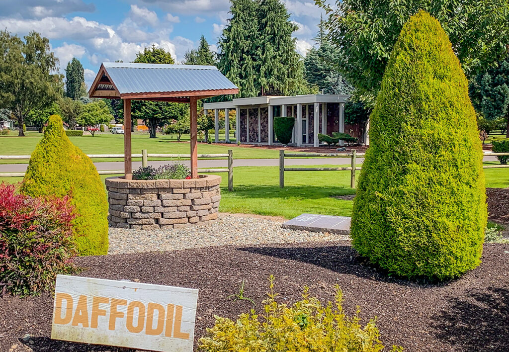 A wishing well with shrubs around it, the Chapel Mausoleum in the background and a sign for Daffodils in the foreground.