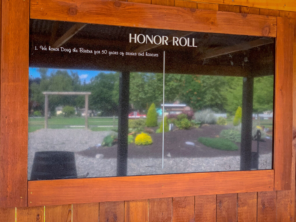 Honor Roll in black granite with white letters etched and a wood frame. Heritage Farm is reflected off the black granite. 