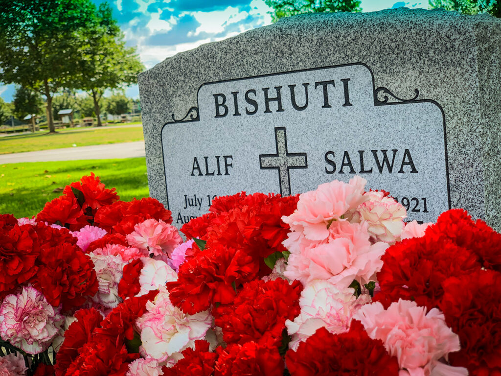 Granite marker for Bishuti, Alif and Salwa with a cross and red and pink carnations in front. 